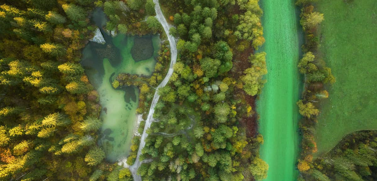 Aerial view of a still green pool and a turquoise river winding through autumn woodland