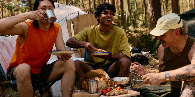 Friends sharing a meal and laughing at a campsite in a pine forest, illustrating AEVUM's energy production pillar.