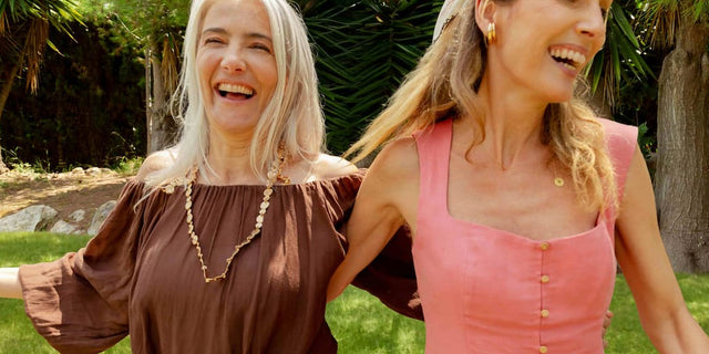 Two women laughing arm in arm in a sunny garden
